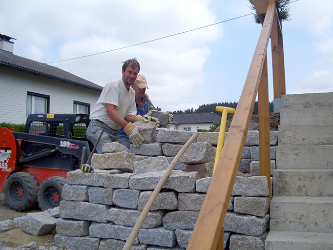 Gerald Berger und ein Kollege bei der Errichtung einer Granitsteinmauer vorm Haus