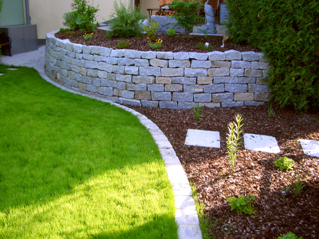 Granitsteinmauer mit Pflanzen und Rasenfläche